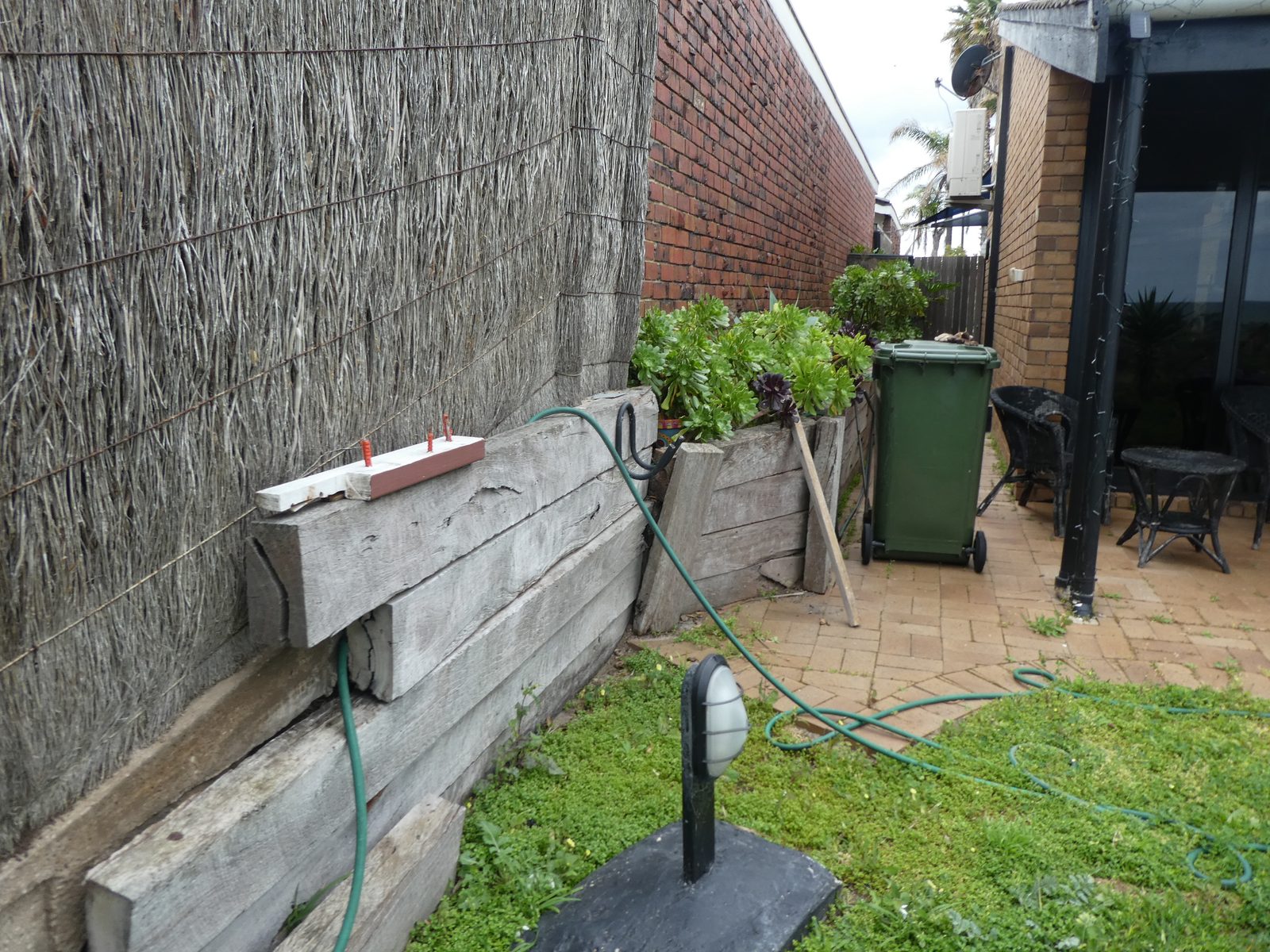 Leaning timber sleeper retaining wall beside a brick boundary